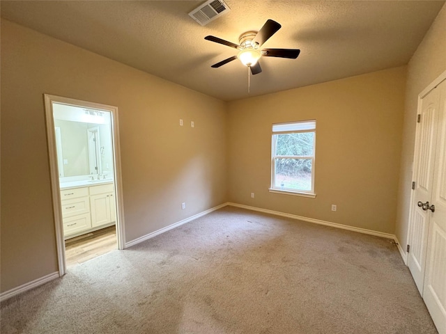 unfurnished bedroom with ceiling fan, ensuite bath, sink, a textured ceiling, and light carpet