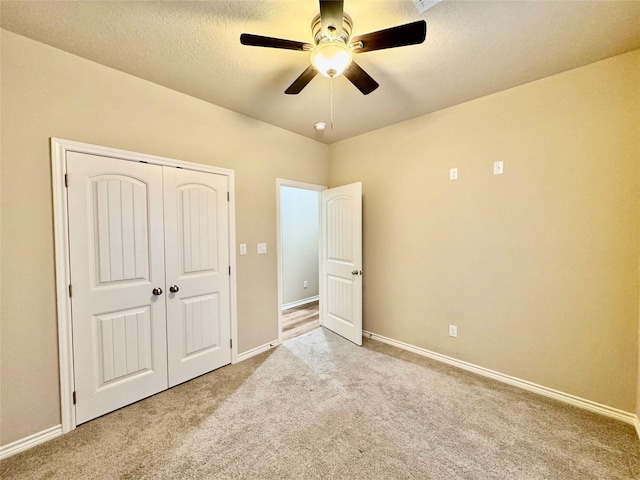 unfurnished bedroom with light carpet, ceiling fan, a closet, and a textured ceiling