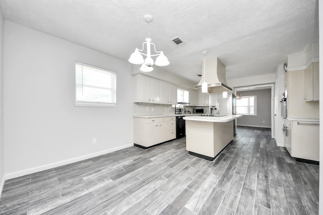 kitchen featuring pendant lighting, island range hood, white cabinets, appliances with stainless steel finishes, and a kitchen island