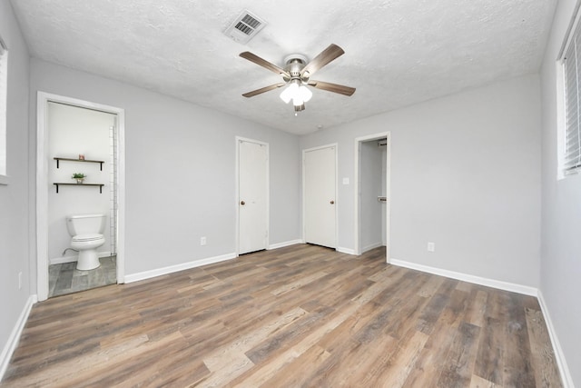 unfurnished bedroom featuring connected bathroom, ceiling fan, dark wood-type flooring, and a textured ceiling