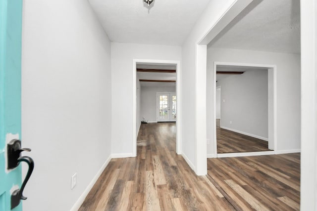 corridor with beam ceiling, french doors, a textured ceiling, and hardwood / wood-style flooring