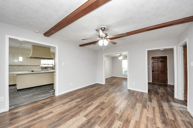 unfurnished living room with beam ceiling, ceiling fan, wood-type flooring, and a textured ceiling