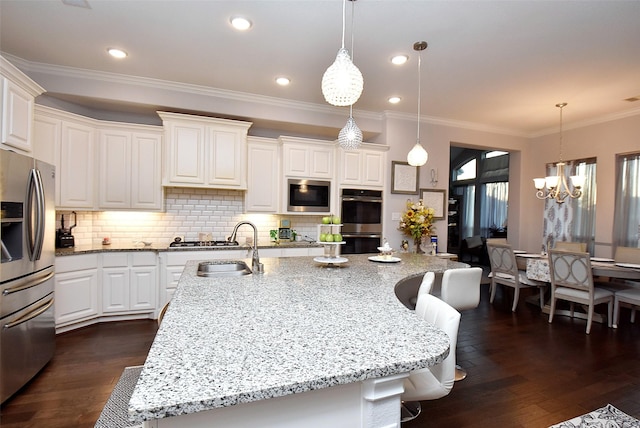 kitchen featuring a kitchen bar, stainless steel appliances, hanging light fixtures, and a center island with sink