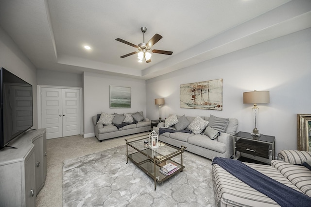 carpeted living room with ceiling fan and a raised ceiling