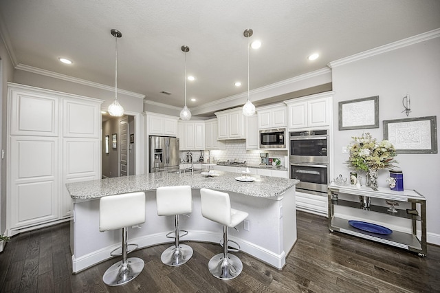 kitchen with appliances with stainless steel finishes, light stone counters, pendant lighting, white cabinets, and an island with sink