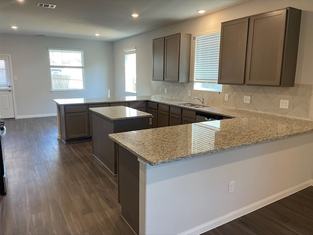 kitchen with kitchen peninsula, light stone countertops, tasteful backsplash, sink, and a kitchen island