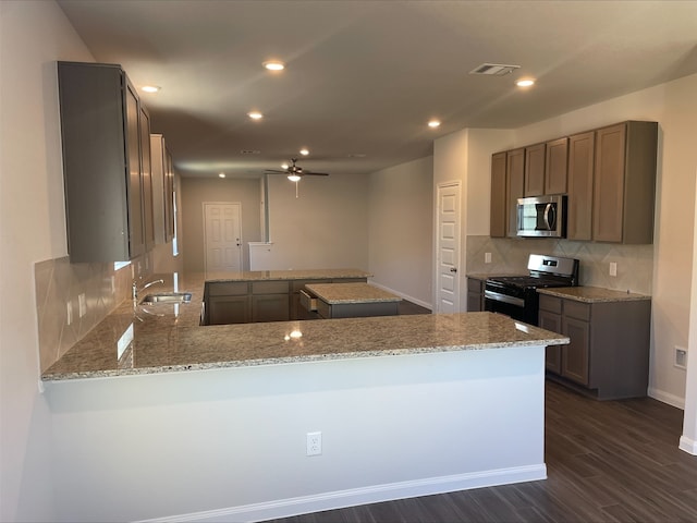 kitchen with kitchen peninsula, appliances with stainless steel finishes, dark hardwood / wood-style flooring, light stone counters, and ceiling fan