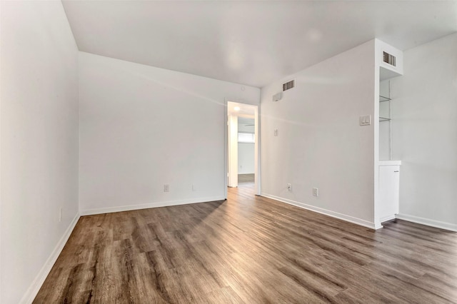 spare room with built in shelves and dark wood-type flooring