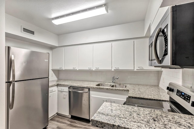 kitchen with light stone countertops, stainless steel appliances, white cabinetry, and sink