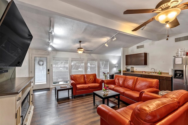 living room with dark wood-type flooring, track lighting, sink, vaulted ceiling, and a textured ceiling