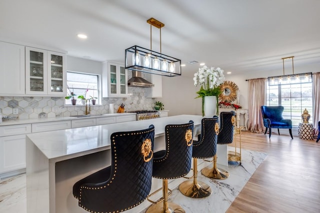 kitchen featuring a center island, a kitchen breakfast bar, wall chimney range hood, sink, and white cabinetry