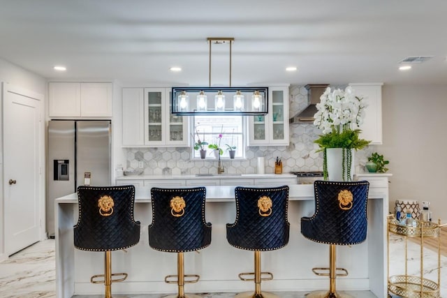 kitchen featuring a breakfast bar, white cabinets, sink, hanging light fixtures, and wall chimney exhaust hood