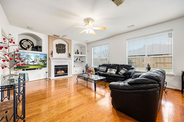 living room with wood-type flooring, a textured ceiling, ceiling fan, and built in shelves