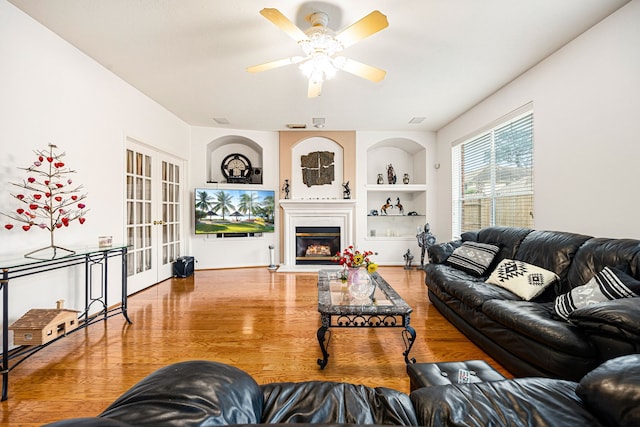 living room featuring hardwood / wood-style flooring, built in features, ceiling fan, and french doors