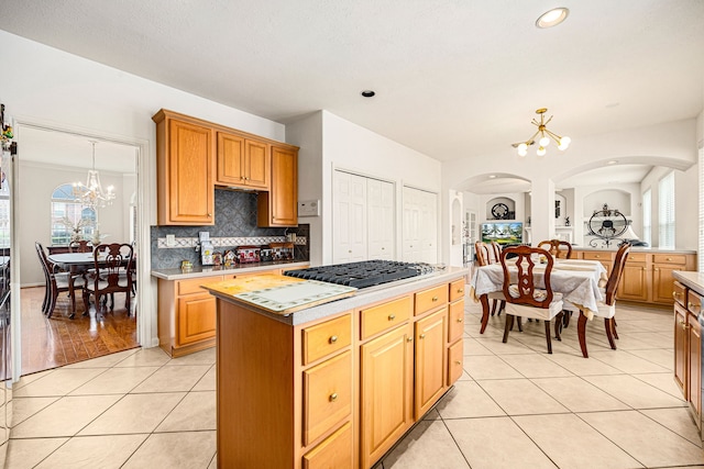 kitchen featuring light tile patterned floors, a center island, tasteful backsplash, a notable chandelier, and stainless steel gas cooktop