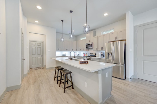 kitchen with sink, pendant lighting, a kitchen island with sink, a breakfast bar, and appliances with stainless steel finishes