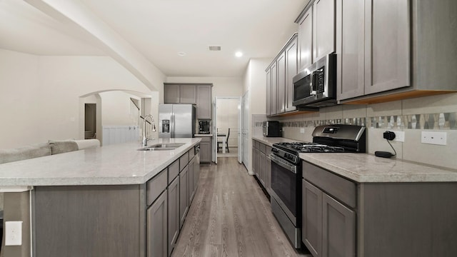 kitchen with gray cabinetry, sink, an island with sink, light hardwood / wood-style floors, and appliances with stainless steel finishes