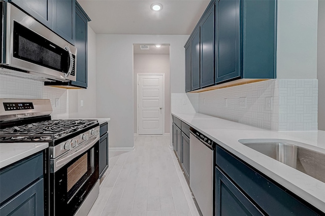 kitchen featuring backsplash, blue cabinetry, appliances with stainless steel finishes, and light hardwood / wood-style flooring