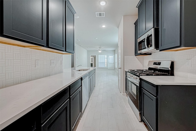 kitchen featuring sink, light hardwood / wood-style flooring, ceiling fan, decorative backsplash, and stainless steel appliances