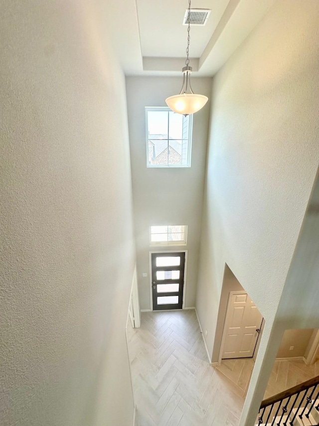 foyer with a high ceiling, a tray ceiling, and light parquet floors