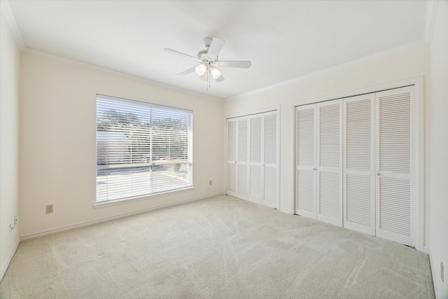 unfurnished bedroom with light carpet, multiple closets, ceiling fan, and ornamental molding