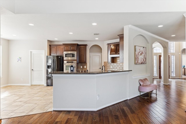 kitchen with decorative backsplash, appliances with stainless steel finishes, light hardwood / wood-style flooring, and dark stone counters