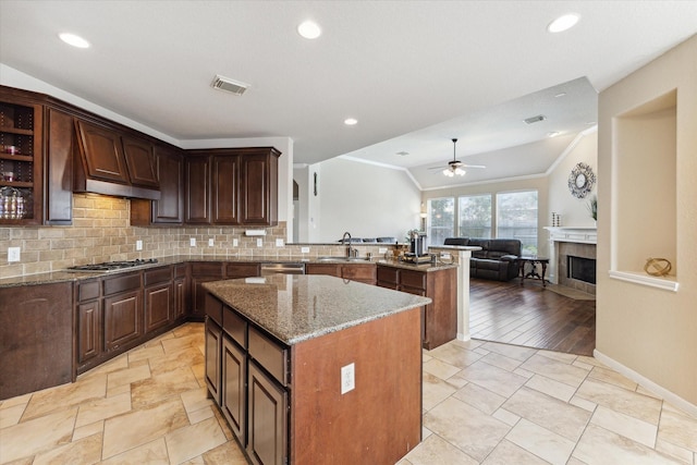 kitchen with sink, light stone countertops, a kitchen island, dark brown cabinetry, and a tiled fireplace