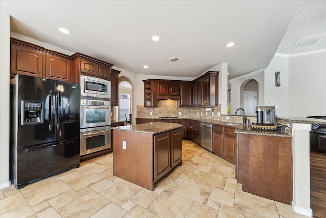 kitchen featuring a center island, sink, kitchen peninsula, dark stone countertops, and appliances with stainless steel finishes