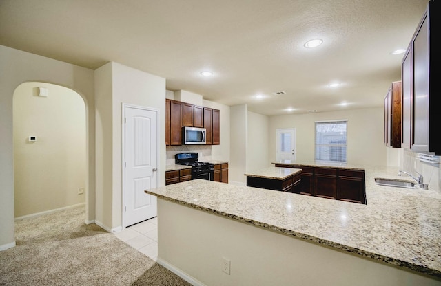 kitchen with black gas stove, light stone countertops, light carpet, sink, and kitchen peninsula