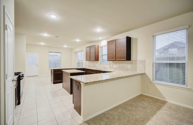 kitchen featuring black range with gas cooktop, light stone countertops, tasteful backsplash, light carpet, and kitchen peninsula