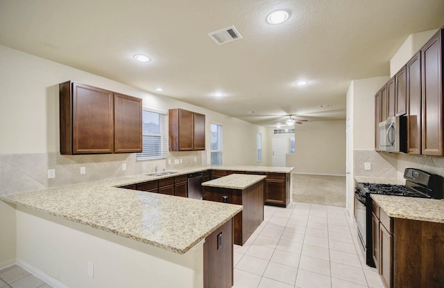 kitchen with kitchen peninsula, backsplash, light stone countertops, a kitchen island, and stainless steel appliances