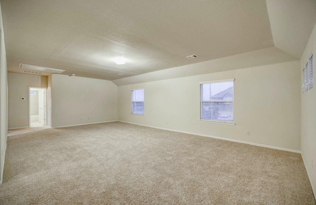 empty room with a textured ceiling, lofted ceiling, and light carpet