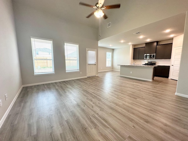 unfurnished living room featuring a towering ceiling, light wood-type flooring, and ceiling fan