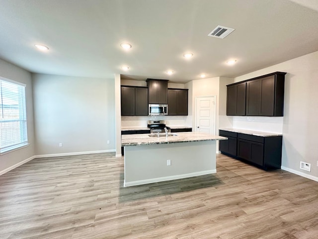 kitchen featuring light stone countertops, light wood-type flooring, a kitchen island with sink, and sink