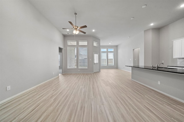 unfurnished living room featuring a high ceiling, light hardwood / wood-style floors, ceiling fan, and sink