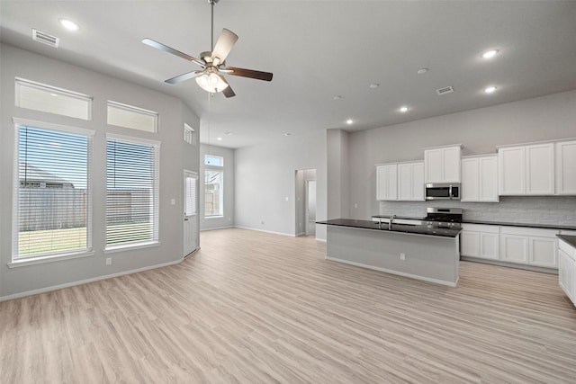 kitchen featuring white cabinets, a center island with sink, decorative backsplash, light wood-type flooring, and appliances with stainless steel finishes