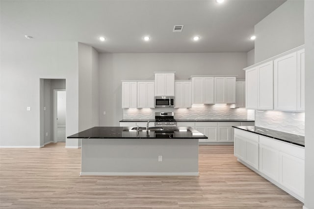 kitchen with appliances with stainless steel finishes, backsplash, a kitchen island with sink, white cabinets, and a high ceiling