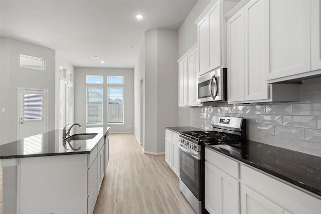 kitchen with white cabinetry, sink, stainless steel appliances, backsplash, and an island with sink