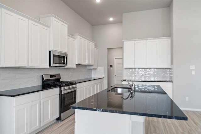 kitchen with sink, light hardwood / wood-style floors, a center island with sink, white cabinets, and appliances with stainless steel finishes