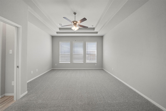 spare room with ceiling fan, a raised ceiling, and light carpet