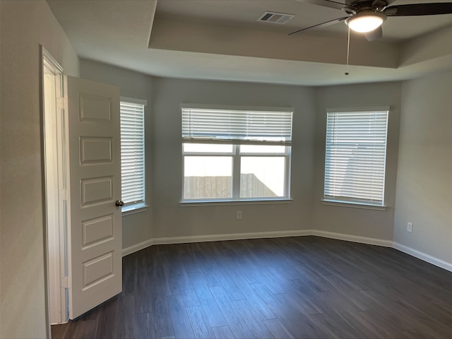 unfurnished room with ceiling fan, dark hardwood / wood-style floors, a raised ceiling, and a wealth of natural light