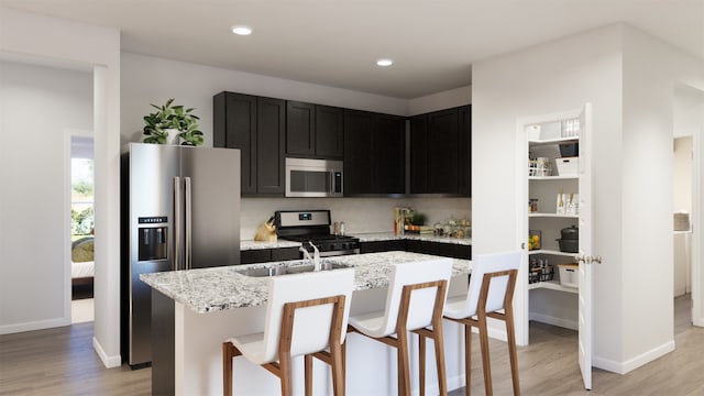 kitchen with a center island with sink, light stone counters, light wood-type flooring, and appliances with stainless steel finishes