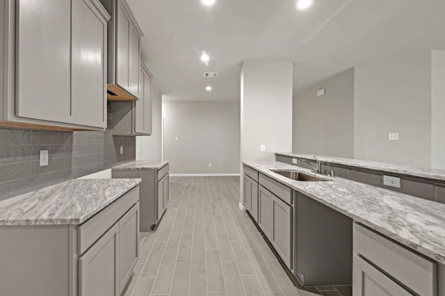 kitchen featuring gray cabinets, light stone counters, and sink