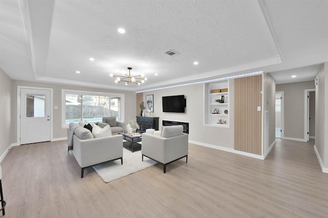 living room featuring light wood-type flooring, an inviting chandelier, a textured ceiling, and a raised ceiling