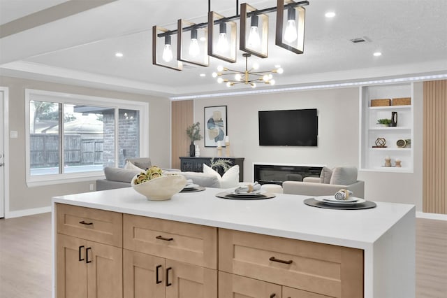 kitchen with pendant lighting, a raised ceiling, light wood-type flooring, light brown cabinets, and a textured ceiling