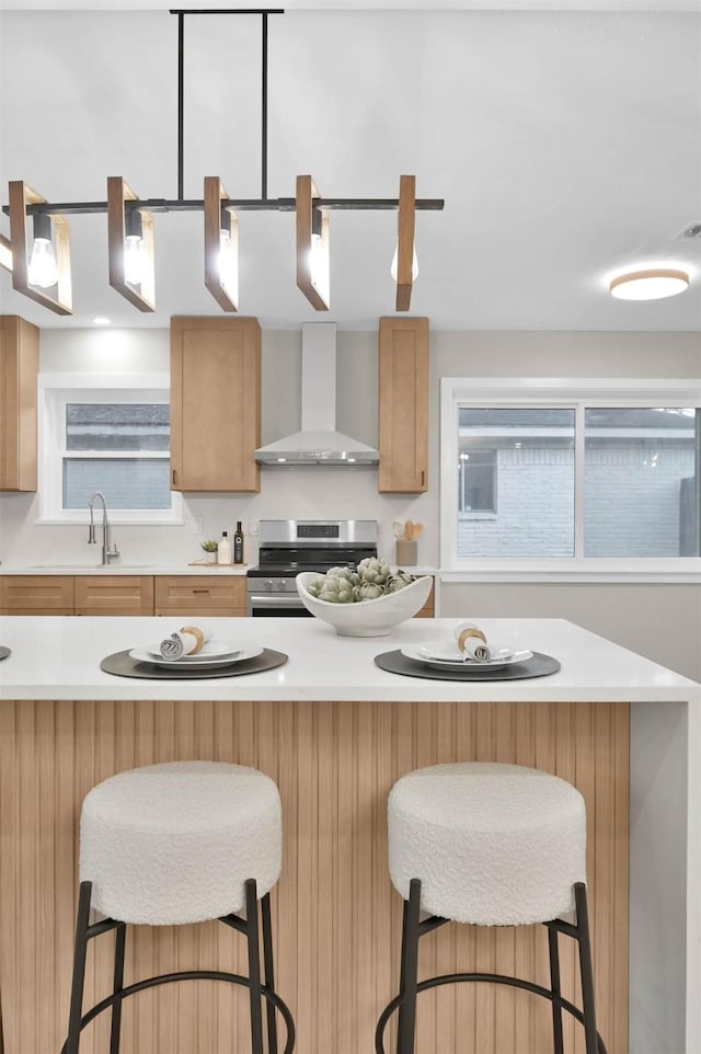 kitchen featuring pendant lighting, wall chimney exhaust hood, a breakfast bar, and stainless steel electric range