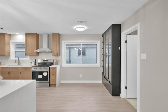 kitchen with wall chimney range hood, sink, light hardwood / wood-style flooring, stainless steel electric stove, and light brown cabinetry