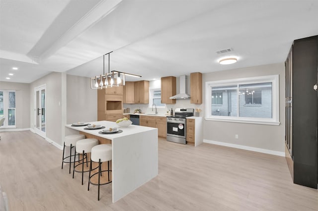 kitchen with light hardwood / wood-style floors, a kitchen bar, stainless steel appliances, wall chimney exhaust hood, and sink