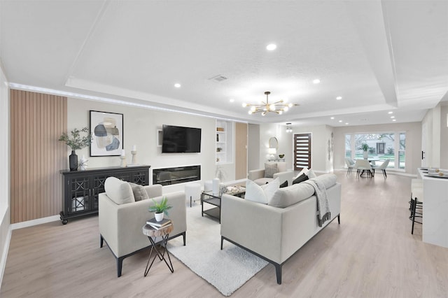 living room featuring an inviting chandelier, light hardwood / wood-style flooring, a raised ceiling, and built in shelves