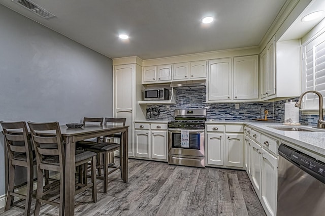 kitchen with sink, decorative backsplash, appliances with stainless steel finishes, light hardwood / wood-style floors, and white cabinetry